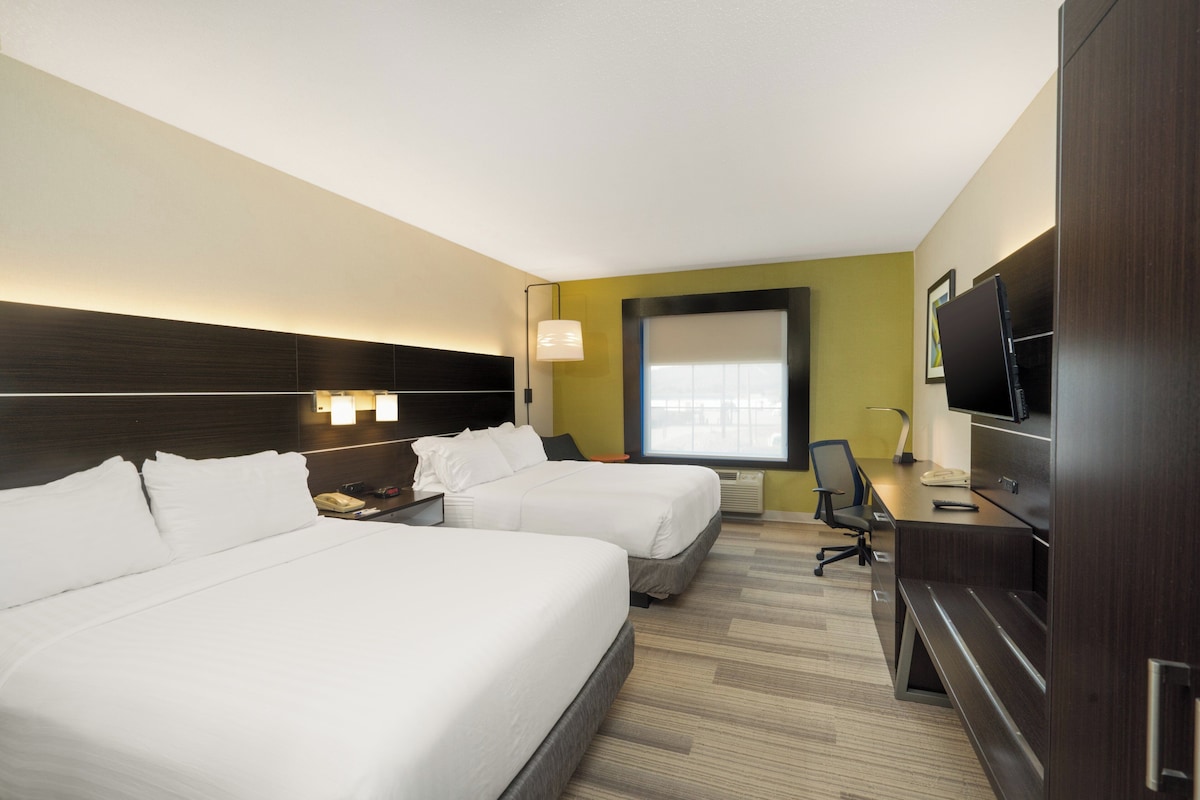 A hotel room with two beds, a desk, a TV, and a window.