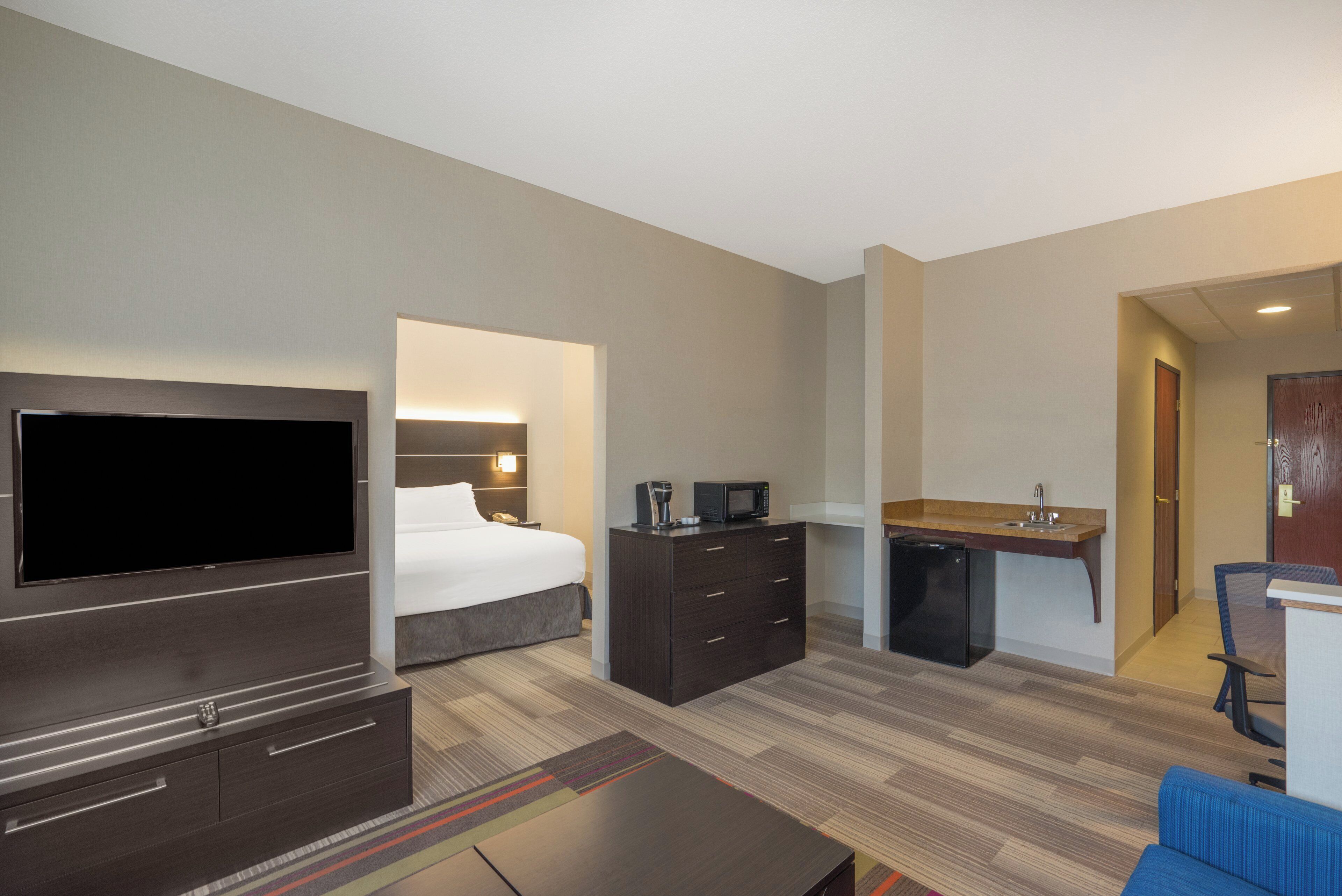 Une chambre d’hôtel avec un lit, une télévision, un bureau doté d’un micro-ondes, un petit réfrigérateur et une chaise bleue.