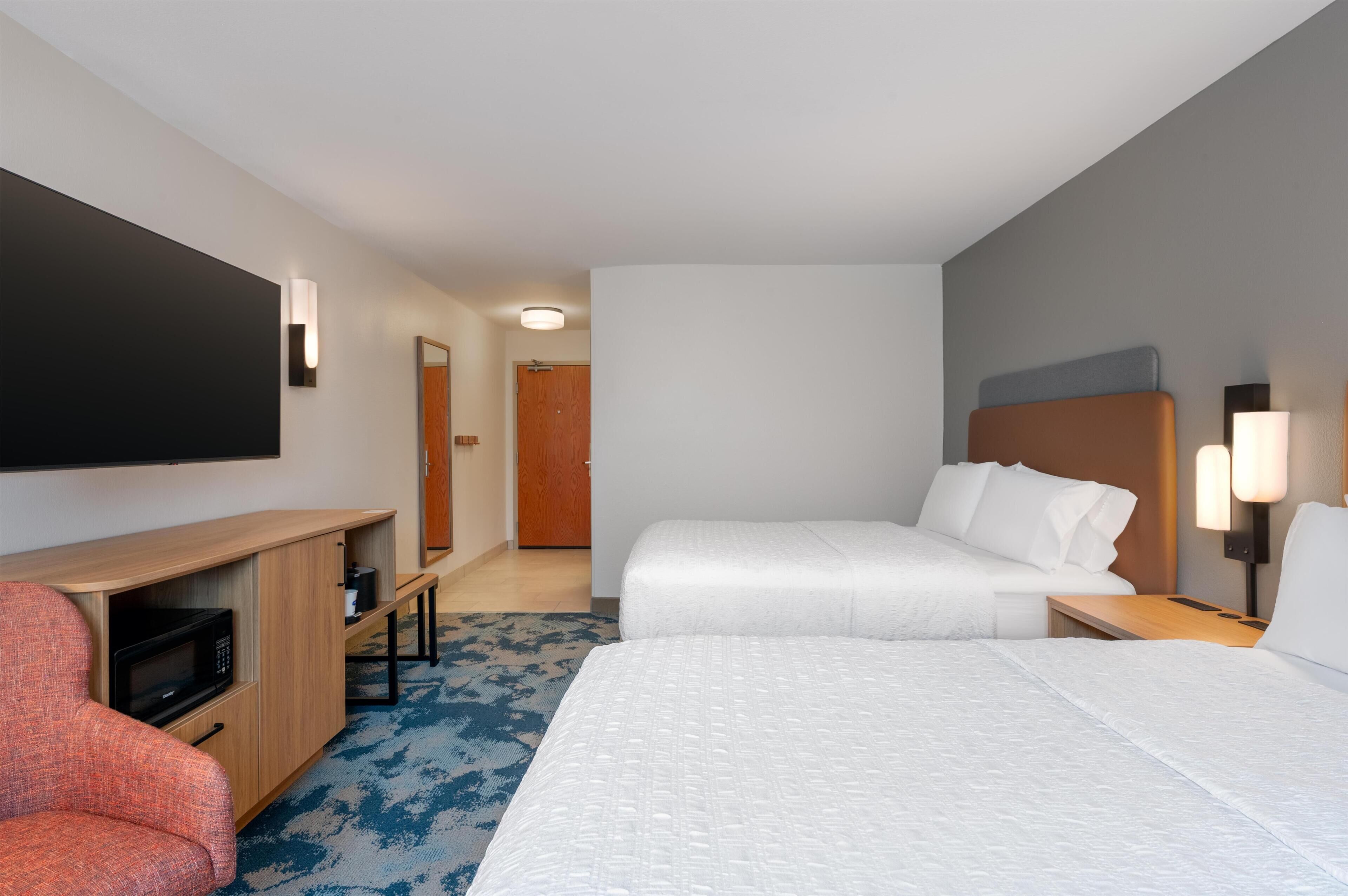 Habitación de hotel con cama, escritorio, silla, televisión de pantalla plana y puerta.