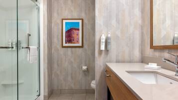 Un baño moderno con cabina de ducha de vidrio, un cuadro con una vista urbana enmarcada en la pared y un tocador con espejo y lavabo.