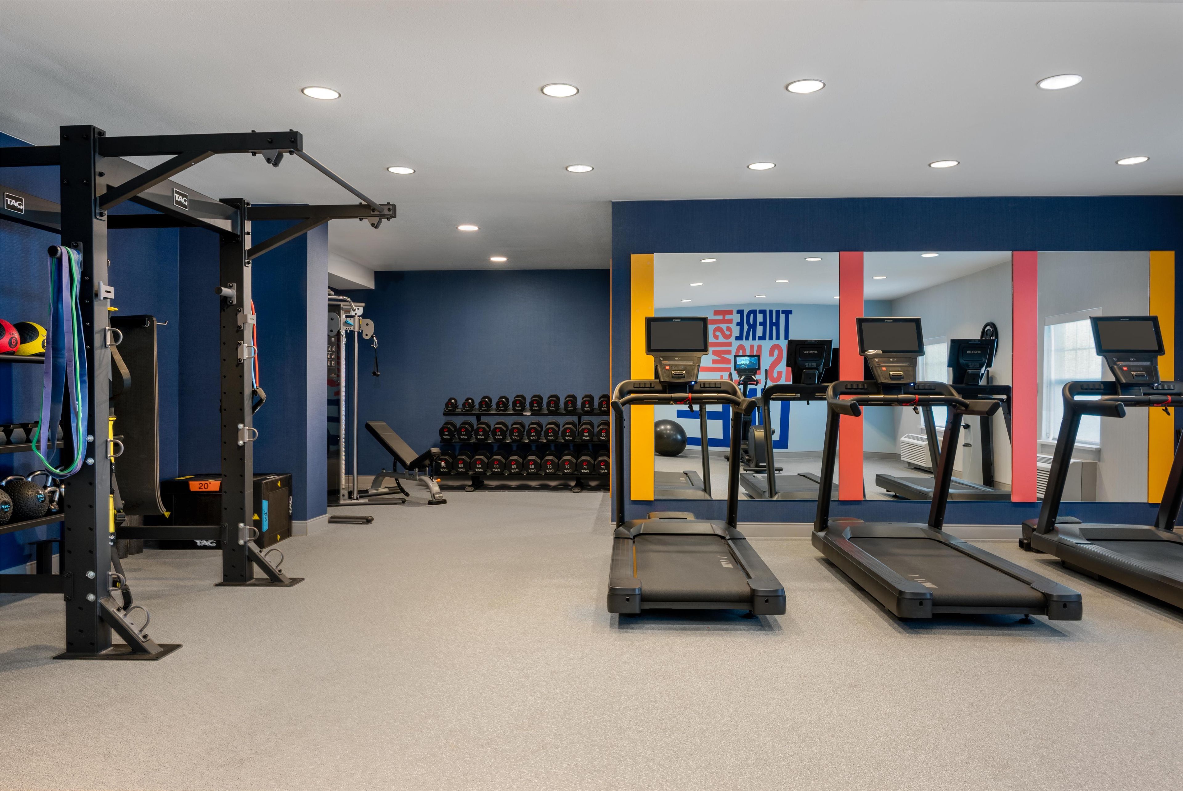 Une salle de sport équipée de tapis de course, d’appareils de musculation et d’haltères.