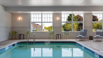 An indoor swimming pool with clear windows, chairs, and a tiled floor.