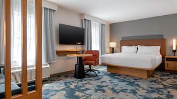 Habitación de hotel con cama, escritorio, silla, televisor y ventana con cortinas.