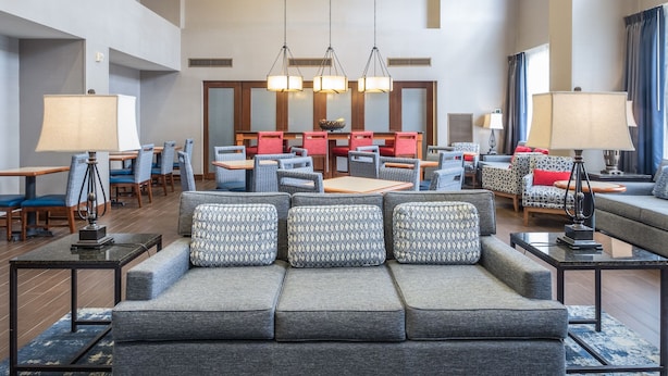 A spacious lobby with a large grey sofa, multiple tables, and hanging chandeliers. - Hampton Inn & Suites Rockland (Thomaston)