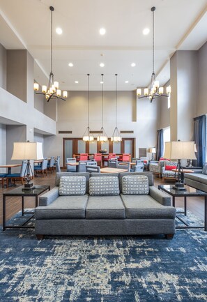 A spacious lobby with a large grey sofa, multiple tables, and hanging chandeliers. - Hampton Inn & Suites Rockland (Thomaston)