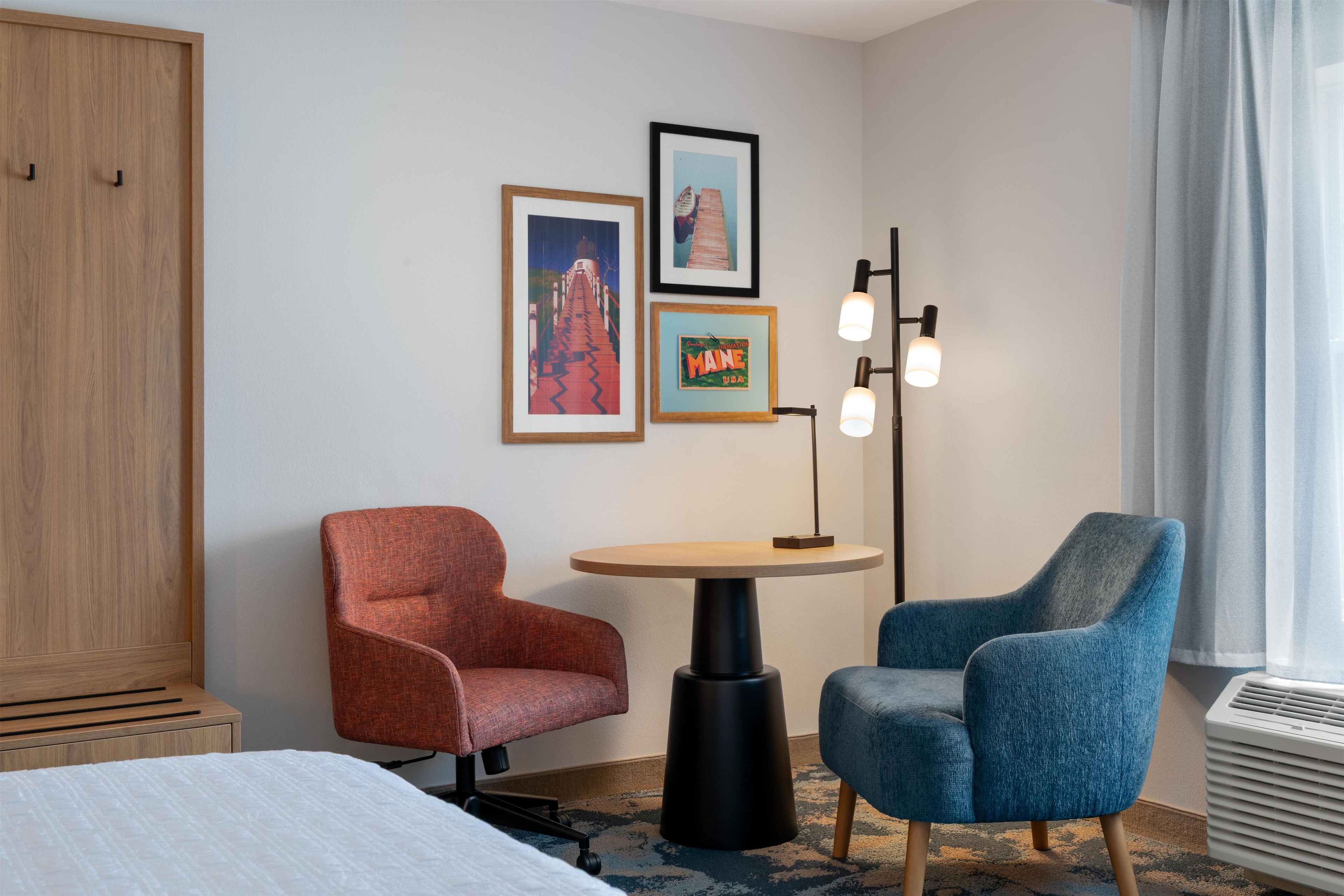 Habitación de hotel con cama, dos sillones, una mesita, lámpara de pie y decoración en la pared.