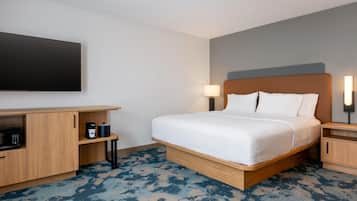 A hotel room with a bed, a flat-screen TV, a coffee maker, and a lamp.