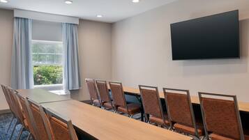 A conference room with a long table, six chairs, a flat-screen TV, and a window with curtains.