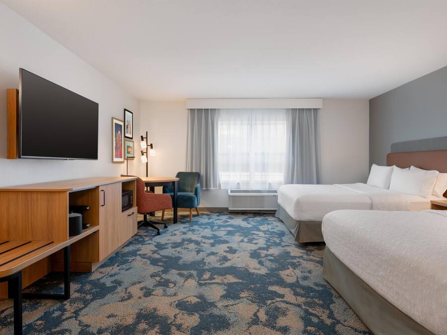 Habitación de hotel con cama, escritorio, silla, televisión y ventana con cortinas.
