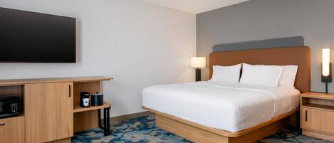 Habitación de hotel con cama, televisor de pantalla plana, cafetera y lámpara.