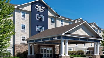Edifício do Hampton Inn & Suites by Hilton, com entrada coberta, fachada de pedra e várias janelas.