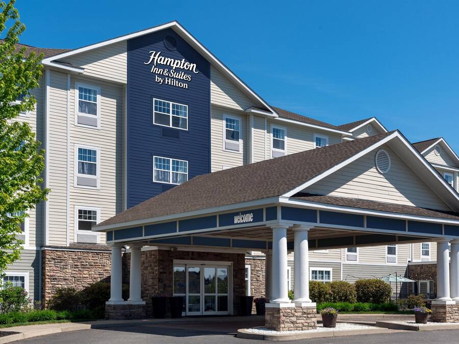 A Hampton Inn & Suites by Hilton building with a covered entrance, stone facade, and multiple windows.