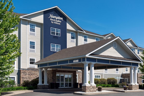 Edificio de Hampton Inn & Suites by Hilton con entrada cubierta, fachada de piedra y varias ventanas.