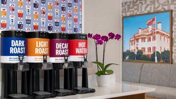 Un espace dédié au café, équipé de quatre distributeurs étiquetés « Mélange torréfié foncé », « Mélange torréfié léger », « Mélange décaféiné » et « Eau chaude ».