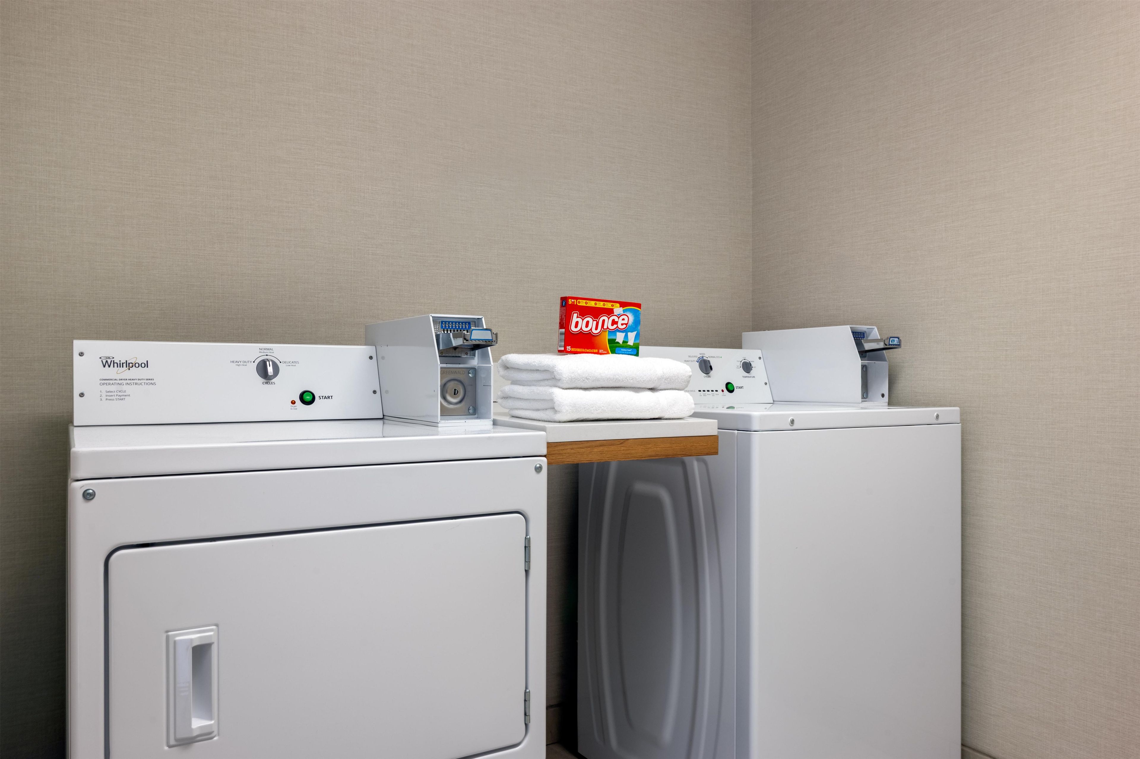 Un espace buanderie équipé d’un lave-linge et d’un sèche-linge Whirlpool, d’une boîte de lessive Bounce et d’une serviette blanche posée sur le sèche-linge.