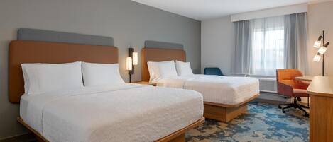 Habitación de hotel con dos camas, un escritorio, una silla y una ventana con cortinas.