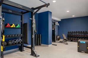 Un gimnasio con equipos de levantamiento de pesas, mancuernas y pelotas de ejercicio.
