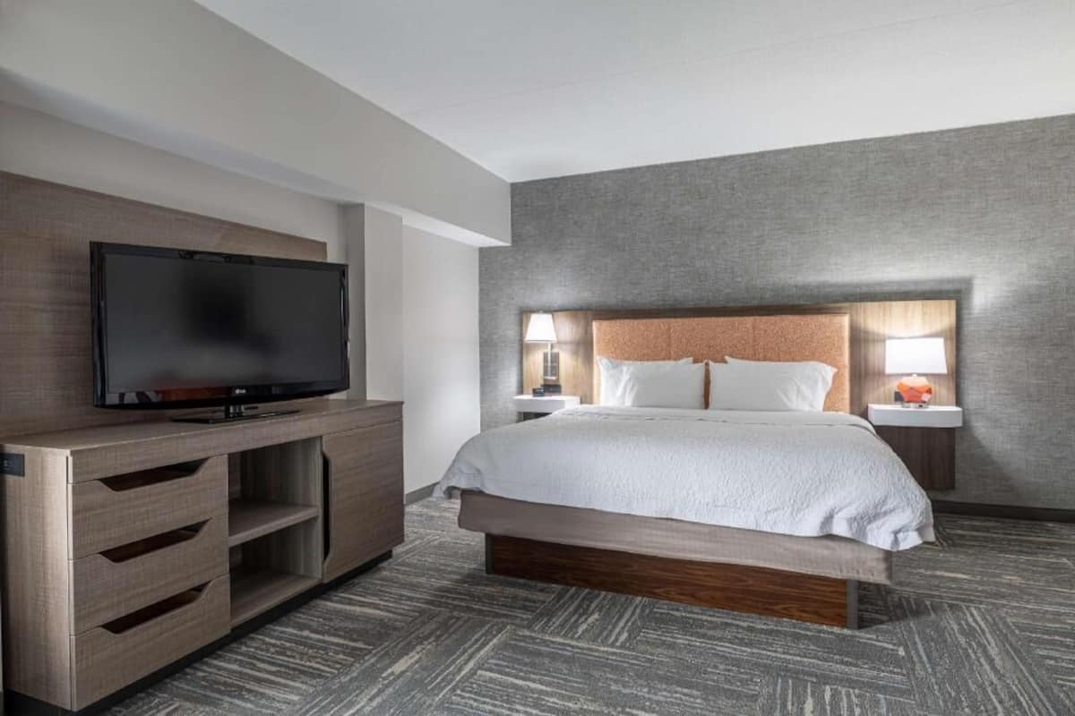 A hotel room with a bed, a TV, a wooden dresser, and a nightstand with lamps.