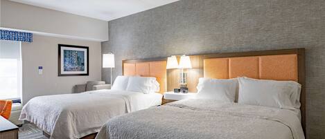 Habitación de hotel con dos camas, una mesita de noche con lámparas, un cuadro enmarcado en la pared y una ventana con vistas.