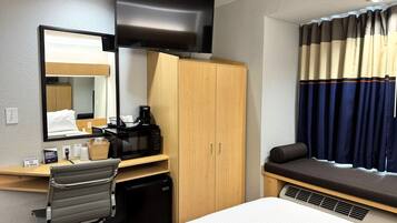 Une chambre d’hôtel comprenant un lit, un bureau avec une chaise, un four à micro-ondes, un petit réfrigérateur, un téléviseur fixé au mur et une fenêtre avec des rideaux.