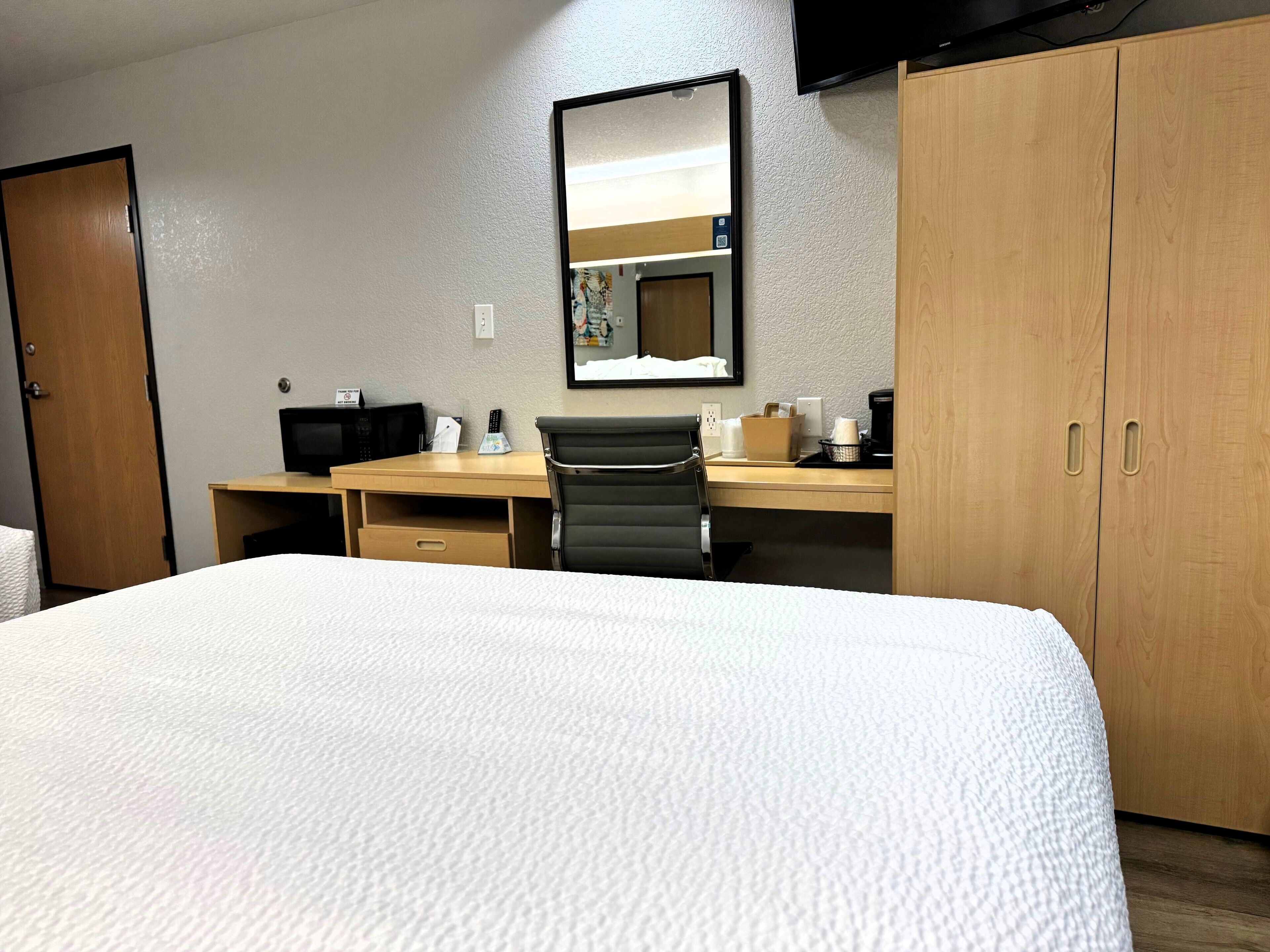 A hotel room with a bed, a desk with a chair, a television, and a wardrobe.