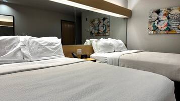 A hotel room with two beds, a large mirror, a wall clock, and a painting.