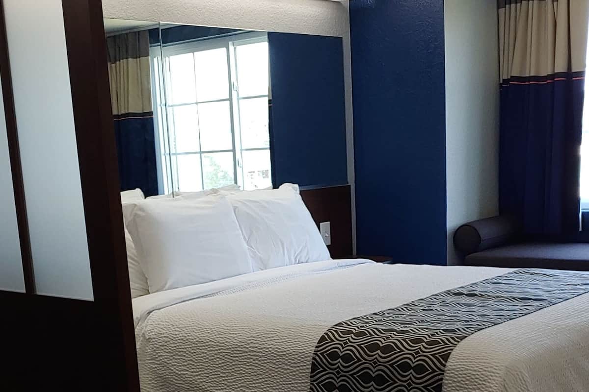 A hotel room with a bed, wooden flooring, a window with curtains, and a blue wall.