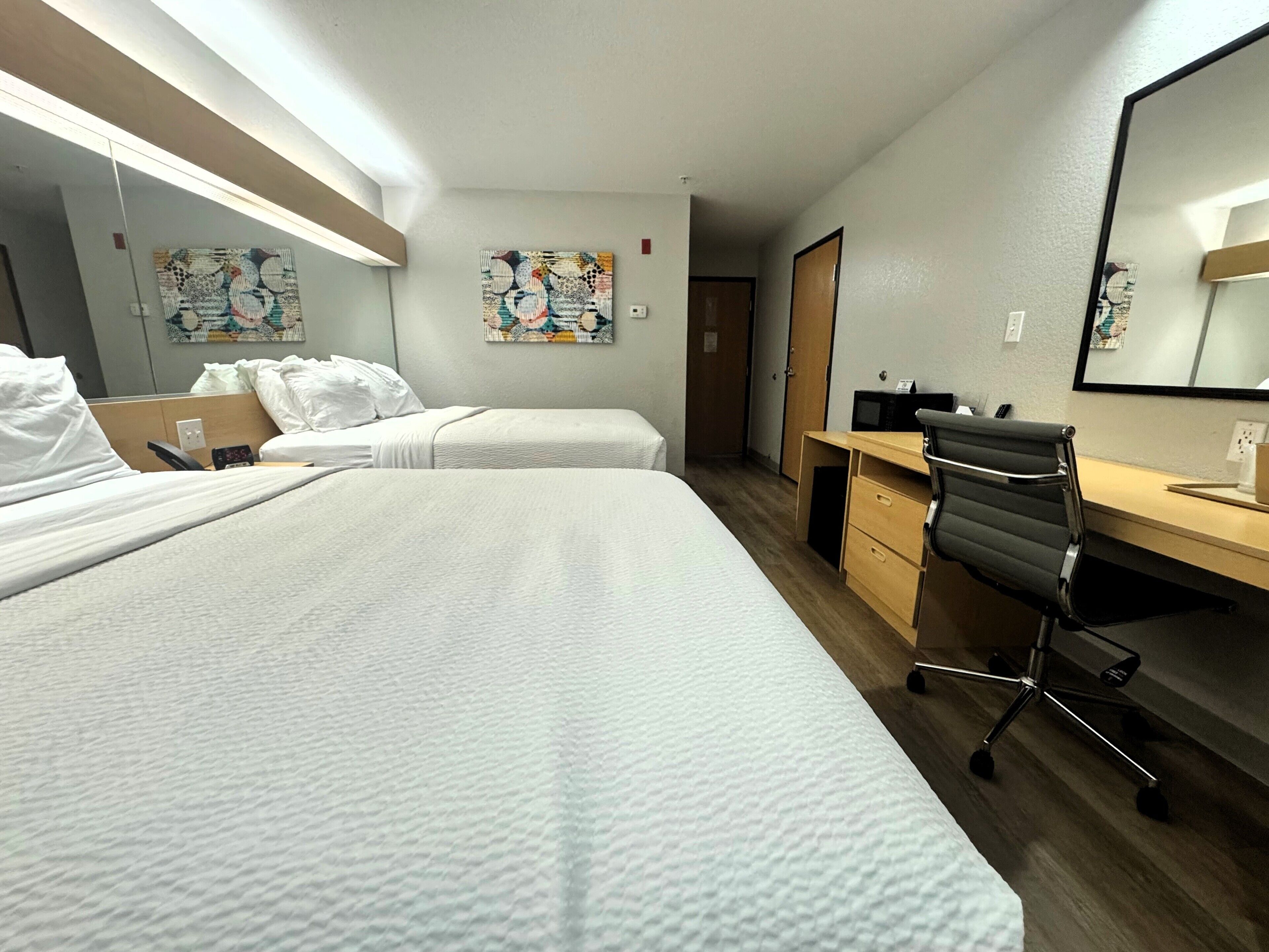 A hotel room with two beds, a desk, a chair, and a large mirror.