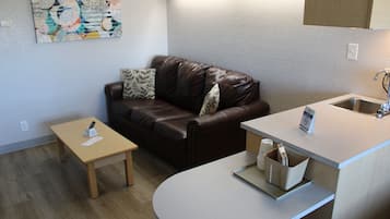 A compact living space with a brown leather sofa, a small wooden table, and a kitchenette area.