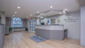 A modern hotel reception area with a reception desk, a clock, and a large window. - Microtel Inn & Suites by Wyndham Albertville (Albertville)