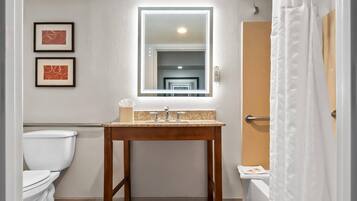 Un baño con tocador de madera, un espejo, dos cuadros enmarcados, un inodoro y una cortina de ducha.