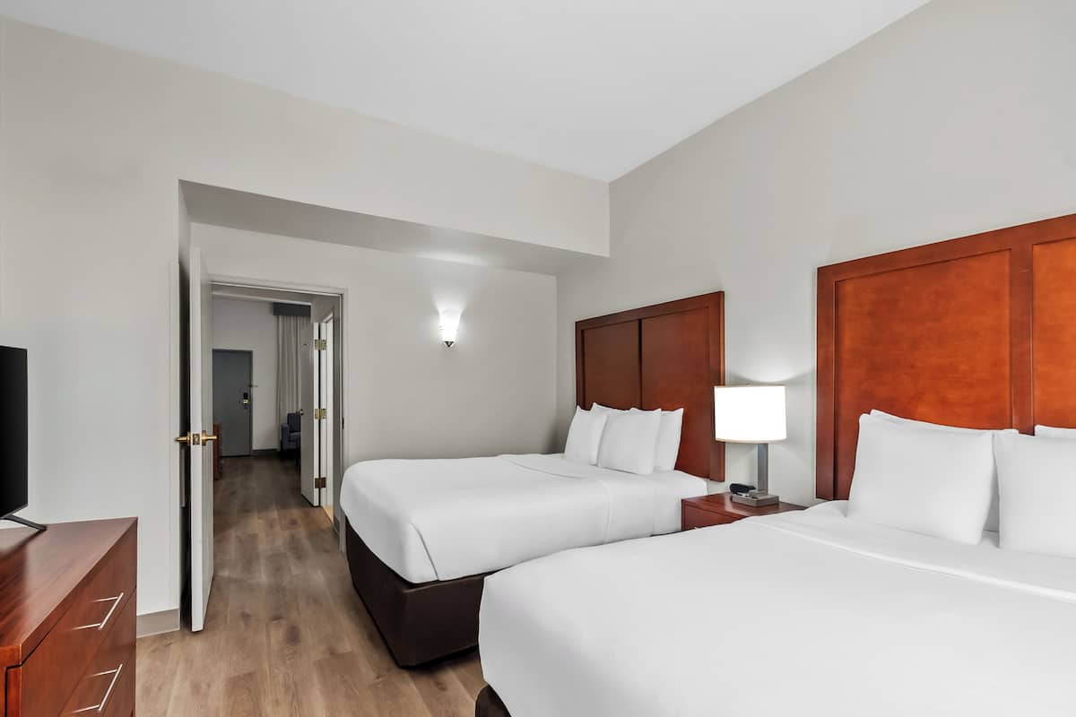 Een hotelkamer met twee bedden, een houten hoofdbord, een nachtkastje met een lamp, een televisie en een houten vloer.