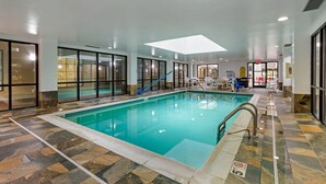 En indendørs swimmingpool med glasvægge, flisegulv og en blå badestige.