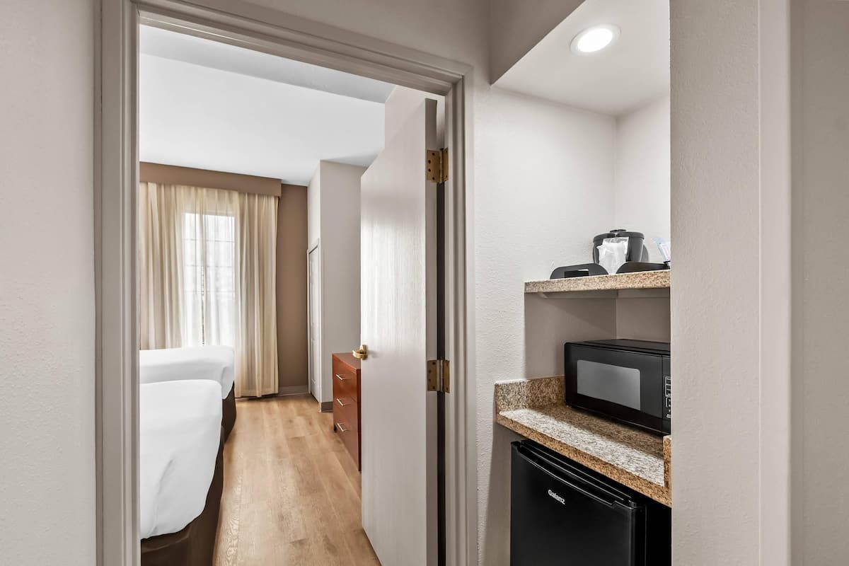 Een hotelkamer met een bed, een kitchenette met een magnetron en een houten vloer.