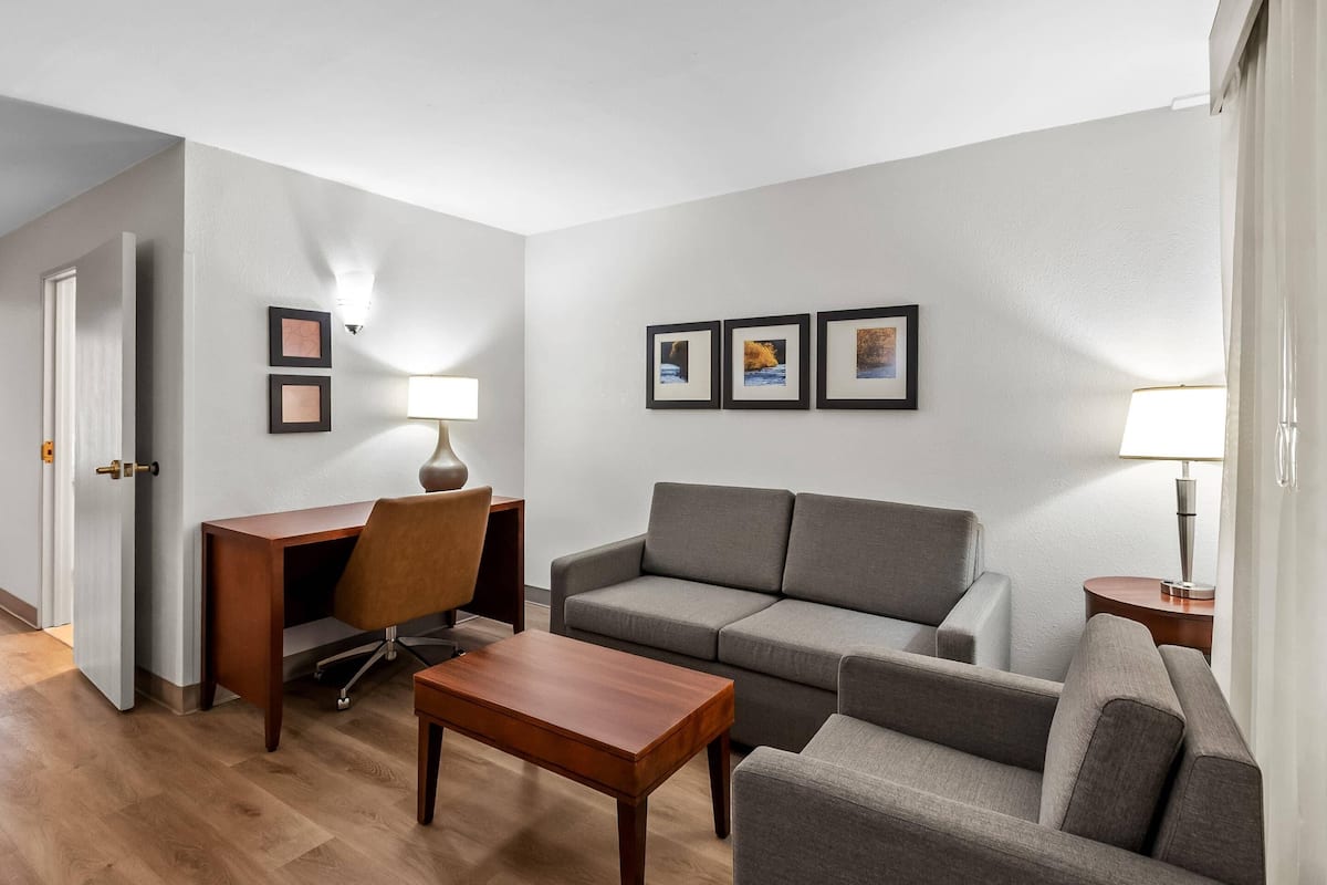 Een moderne woonkamer met een grijze bank, een houten salontafel, een bureau met een stoel en lijstjes met foto’s aan de muur.