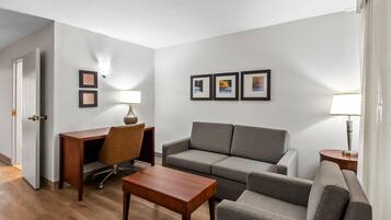 A modern living room with a grey sofa, a wooden coffee table, a desk with a chair, and framed pictures on the wall.