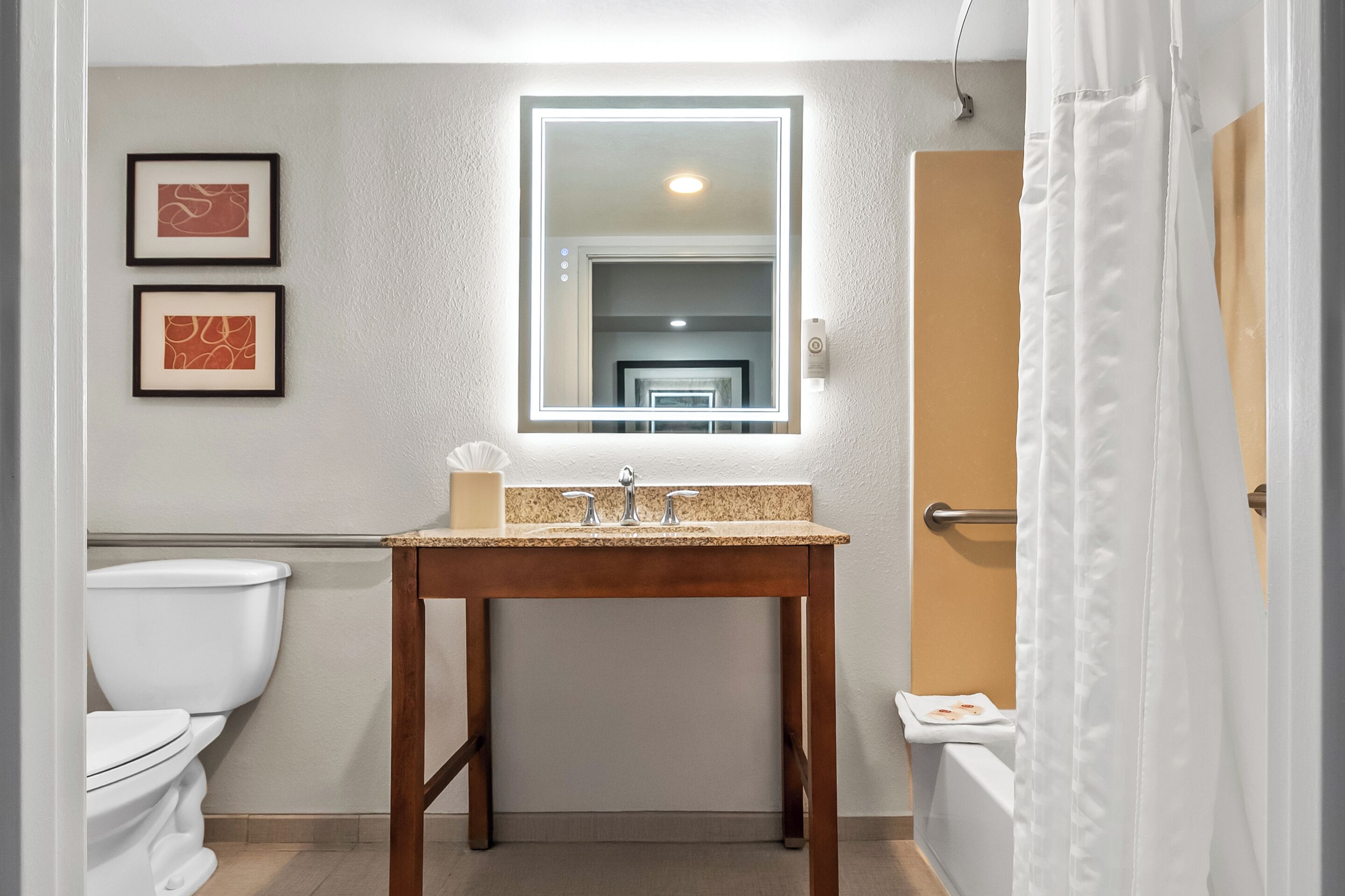 A bathroom with a wooden vanity, a mirror, and two framed artworks on the wall.