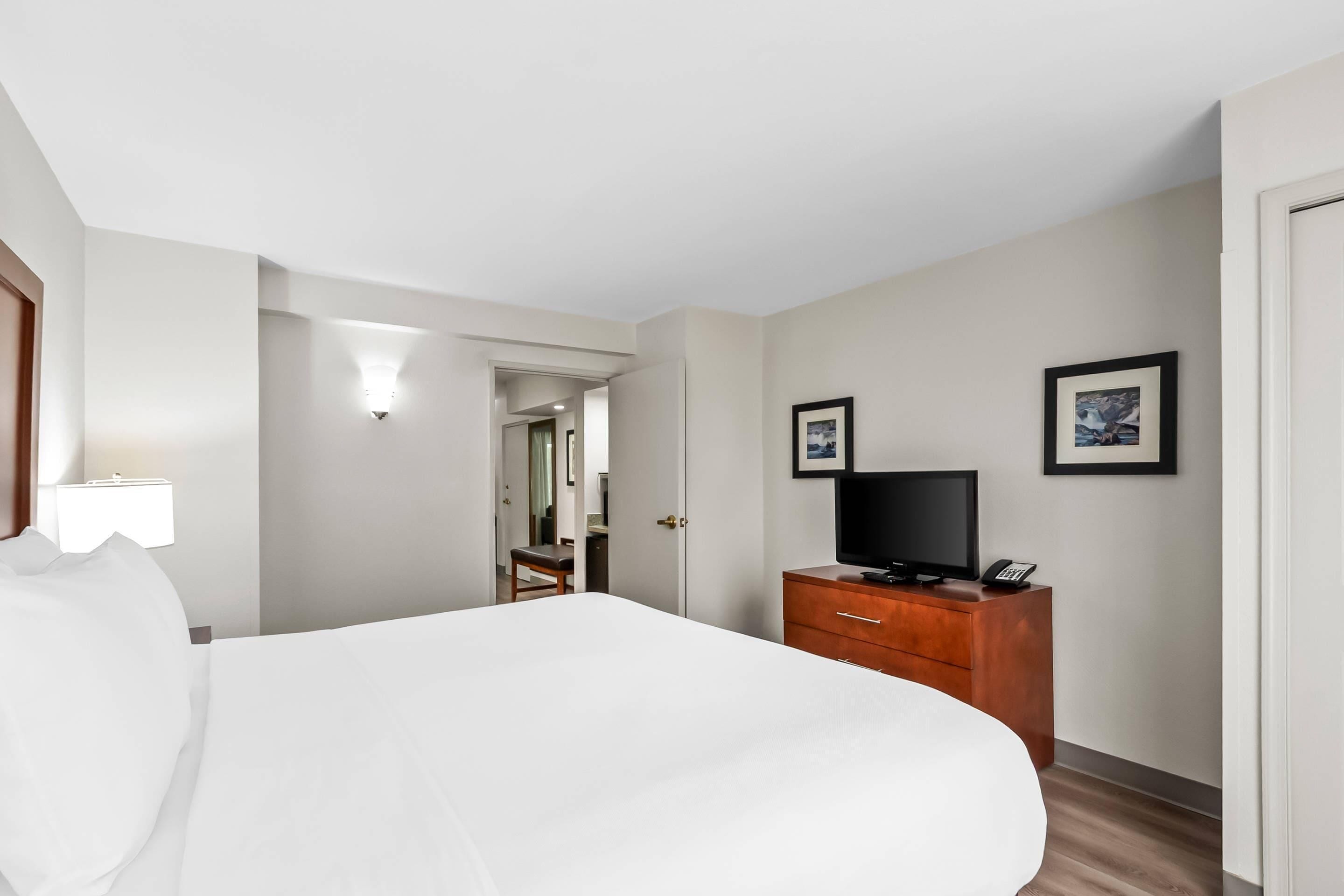 Ein Hotelzimmer mit einem Bett, einem Schminktisch, einem Fernseher und gerahmten Bildern an der Wand.