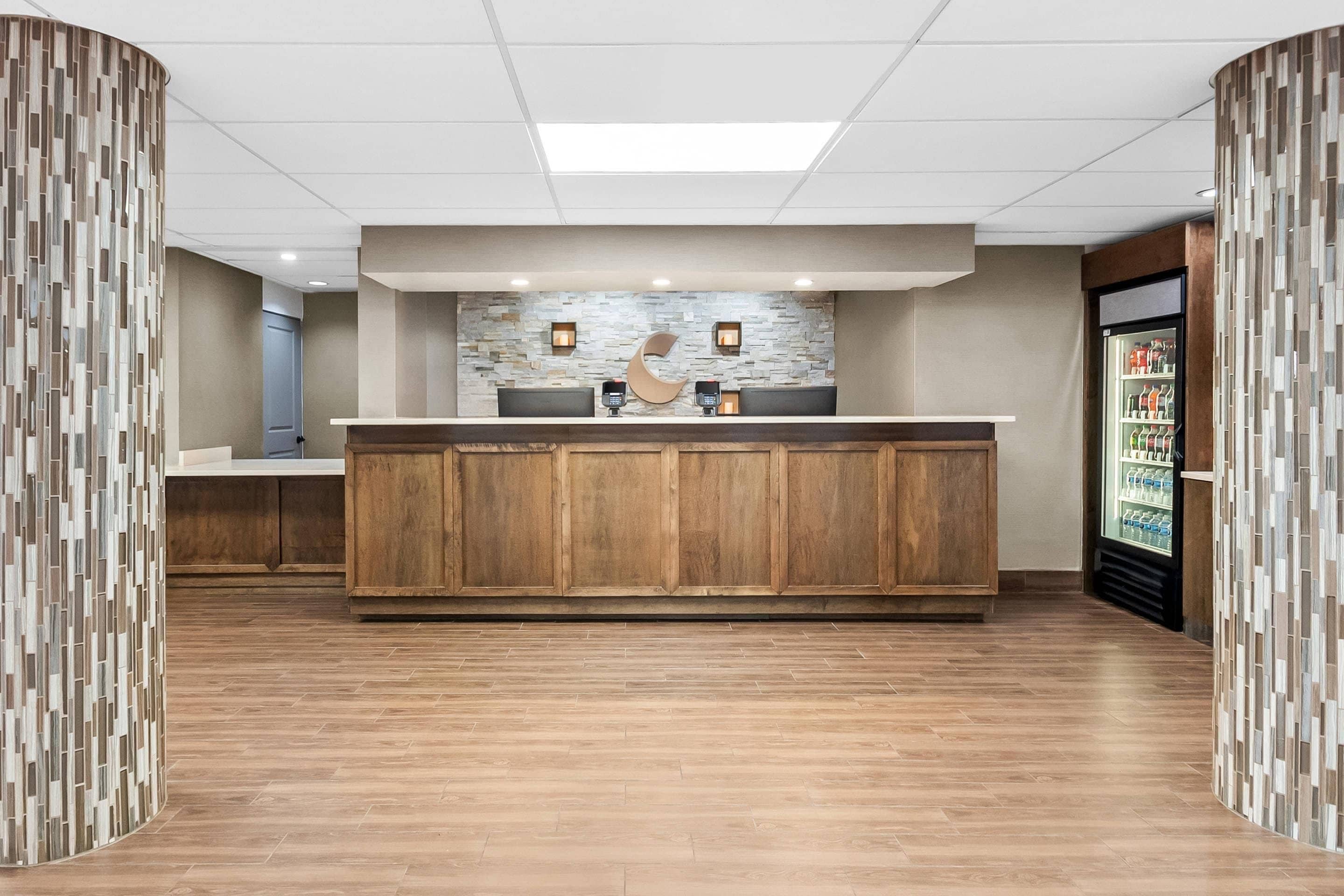 Zona de recepción con mostrador de madera, pared de piedra y un refrigerador lleno de bebidas.