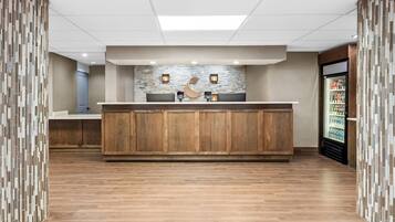 Zona de recepción con mostrador de madera, pared de piedra y un refrigerador lleno de bebidas.