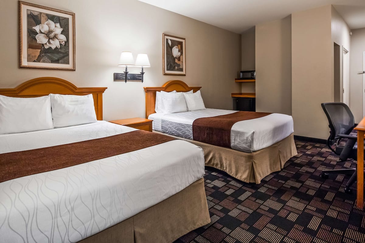 A hotel room with two beds, a desk, and a chair. There are wall-mounted lamps and framed artwork above the beds.