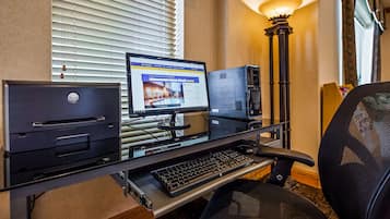 A hotel room with a desktop computer setup including a monitor, keyboard, and printer.