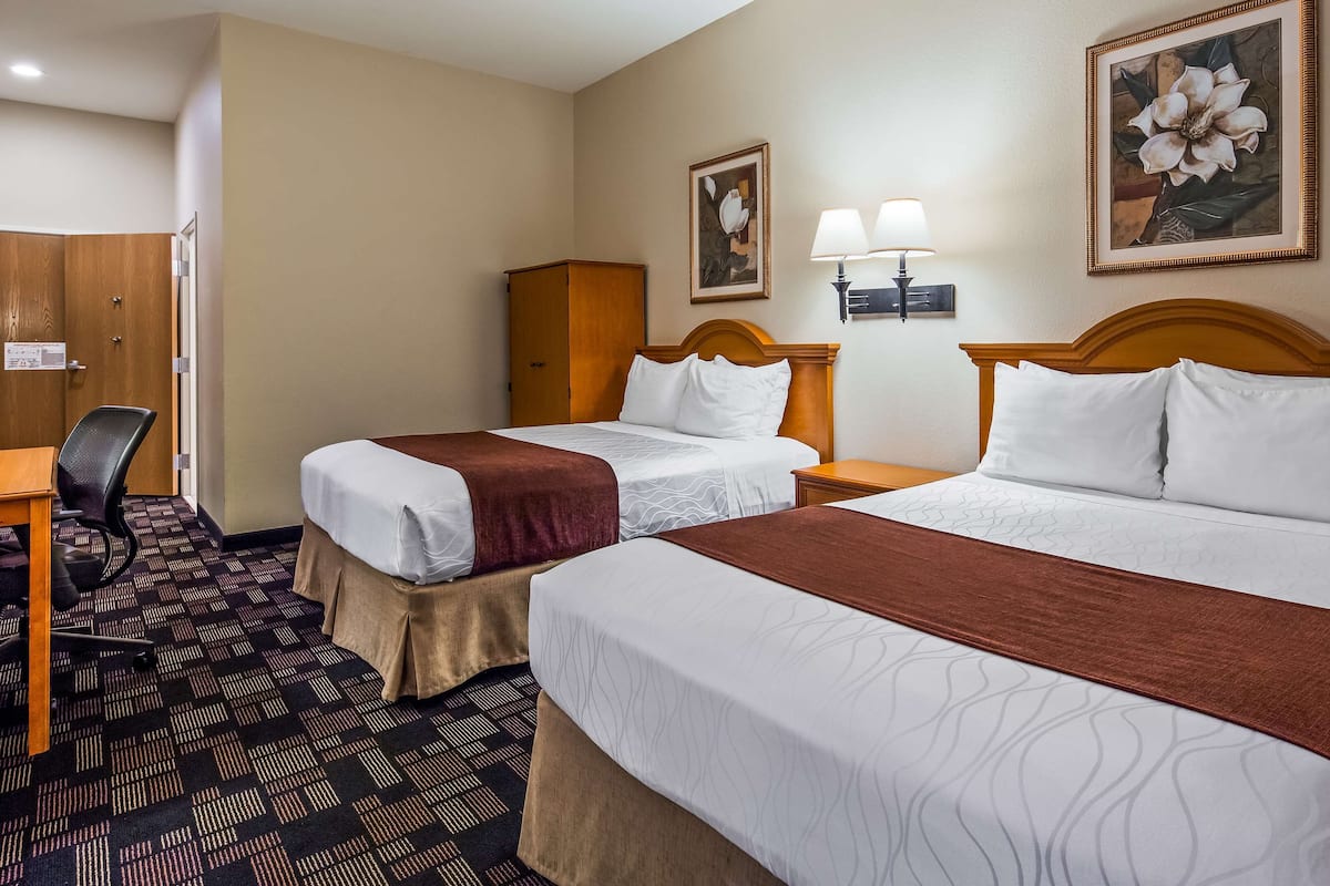 A hotel room with two beds, a desk, a chair, a wardrobe, and two wall-mounted lamps.