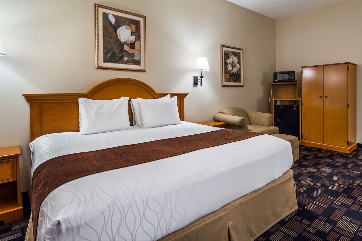 A hotel room with a large bed, a wooden wardrobe, a desk, and a chair.