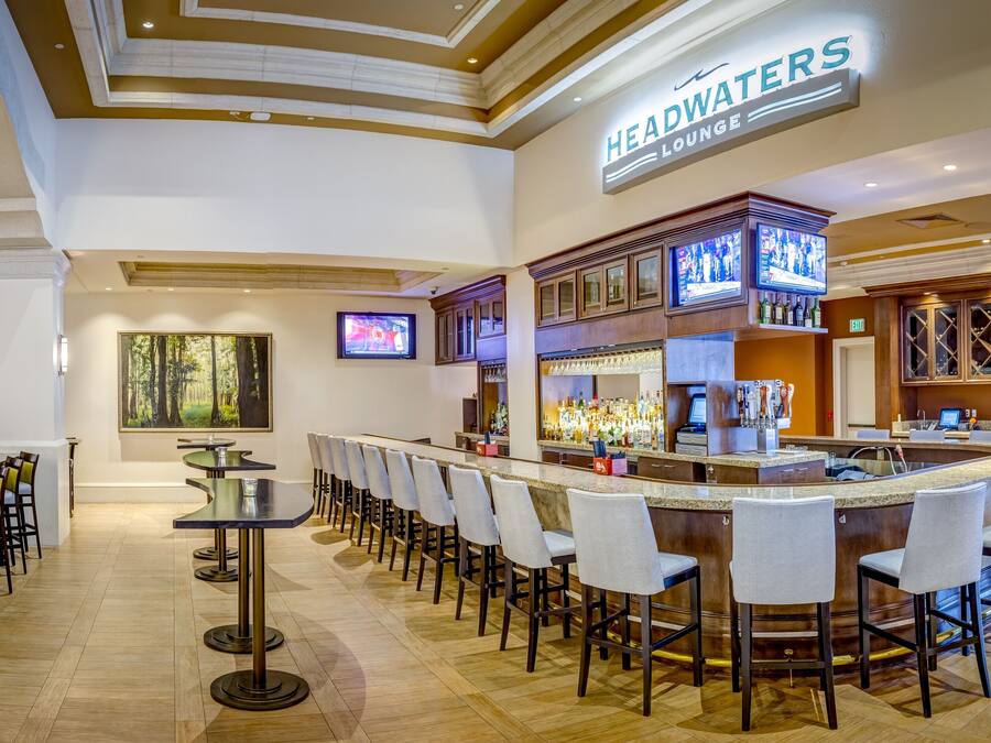 Angolo bar con varie opzioni di seduta, un televisore e un cartello che indica “HEADWATERS LOUNGE”.