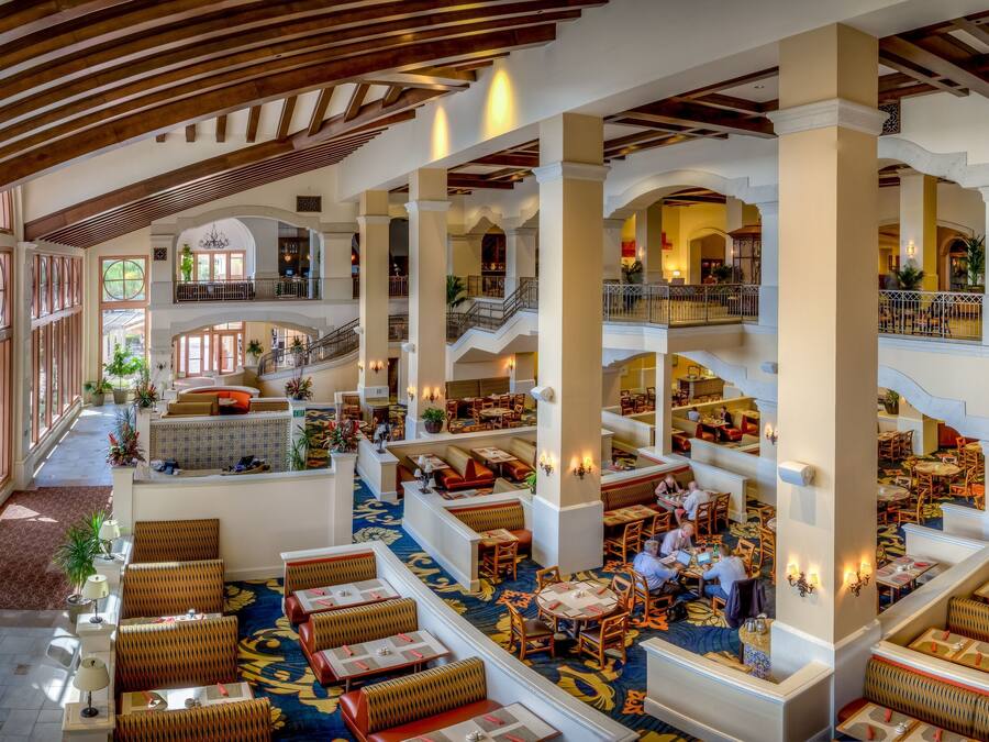 Een ruime hotel lobby met meerdere zithoeken, een centrale trap en grote ramen met uitzicht op de omgeving.