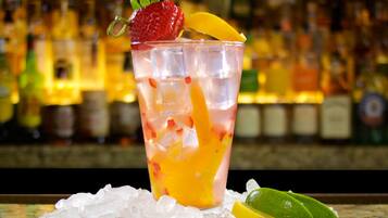 Un cóctel con adorno de frutas sobre una barra con botellas al fondo.