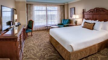 A hotel room with a large bed, a desk with a telephone, a chair, a small table, and a window with curtains.