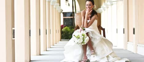 Un pasillo con columnas y una persona con vestido de novia sentada en una silla.