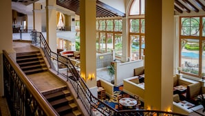 A spacious hotel lobby with a central staircase, multiple seating areas, and large windows offering views of the outdoor area. - Rosen Shingle Creek (Orlando)